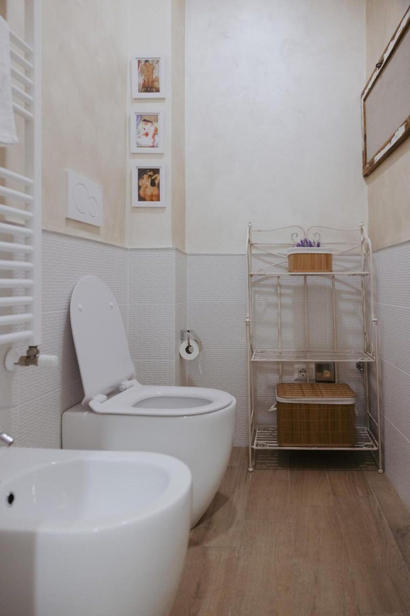 Sanitari del bagno con scaldasalviette a parete, scaffale in ferro battuto bianco e cesto in vimini