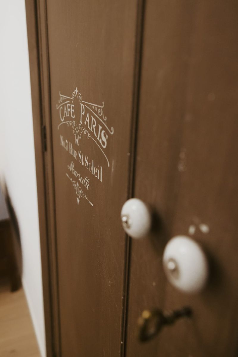 Dettaglio dell’armadio in legno scuro con scritta a stencil e pomelli in ceramica bianca